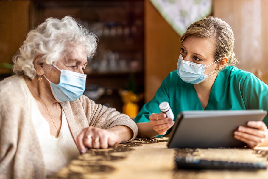 nurse holding medication while discussing with elderly patient