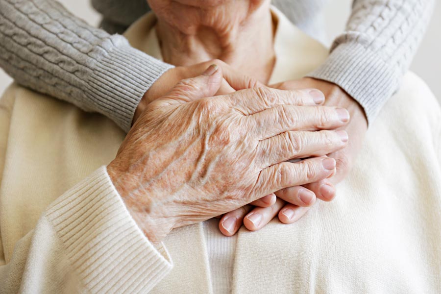 two pairs of hand clasped over elderly person's chest