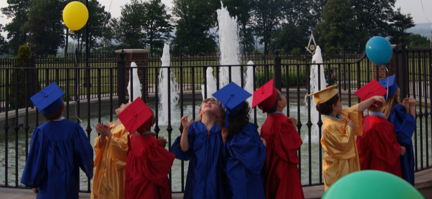 Image of 9 children wearing caps and gowns in primary colors, red blue and gold